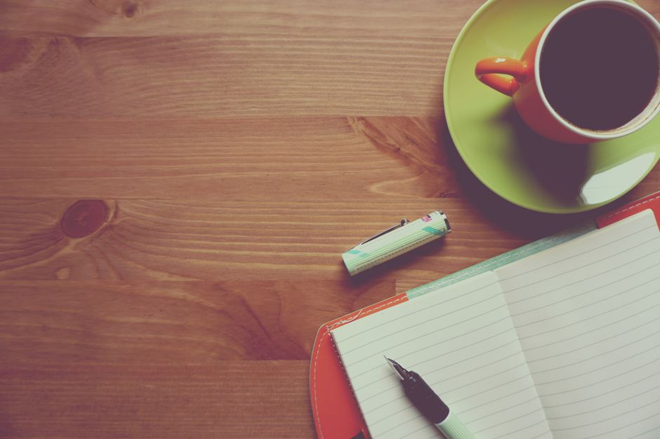 A warm and inviting workspace featuring a cup of coffee, journal, and pen on a wooden table.